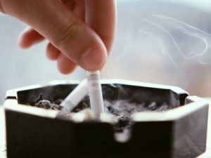 hand-putting-out-a-smoking-cigarette-in-an-ashtray-with-buildings-in-background_ekkppjzn__F0000_500x375